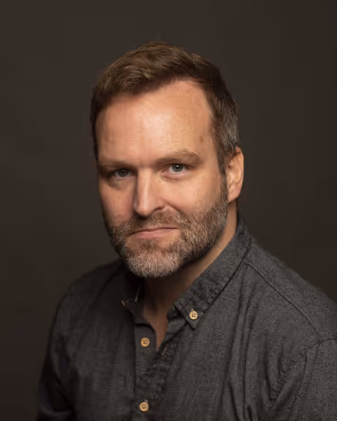Colin Weldon, photographed in a dark grey shirt against a deep olive background